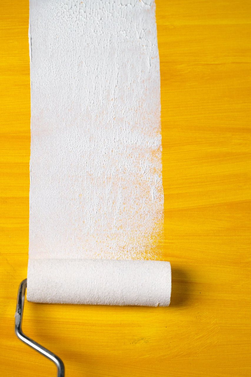 Free A close-up of a paint roller creating a white stripe on a vibrant yellow surface. Stock Photo