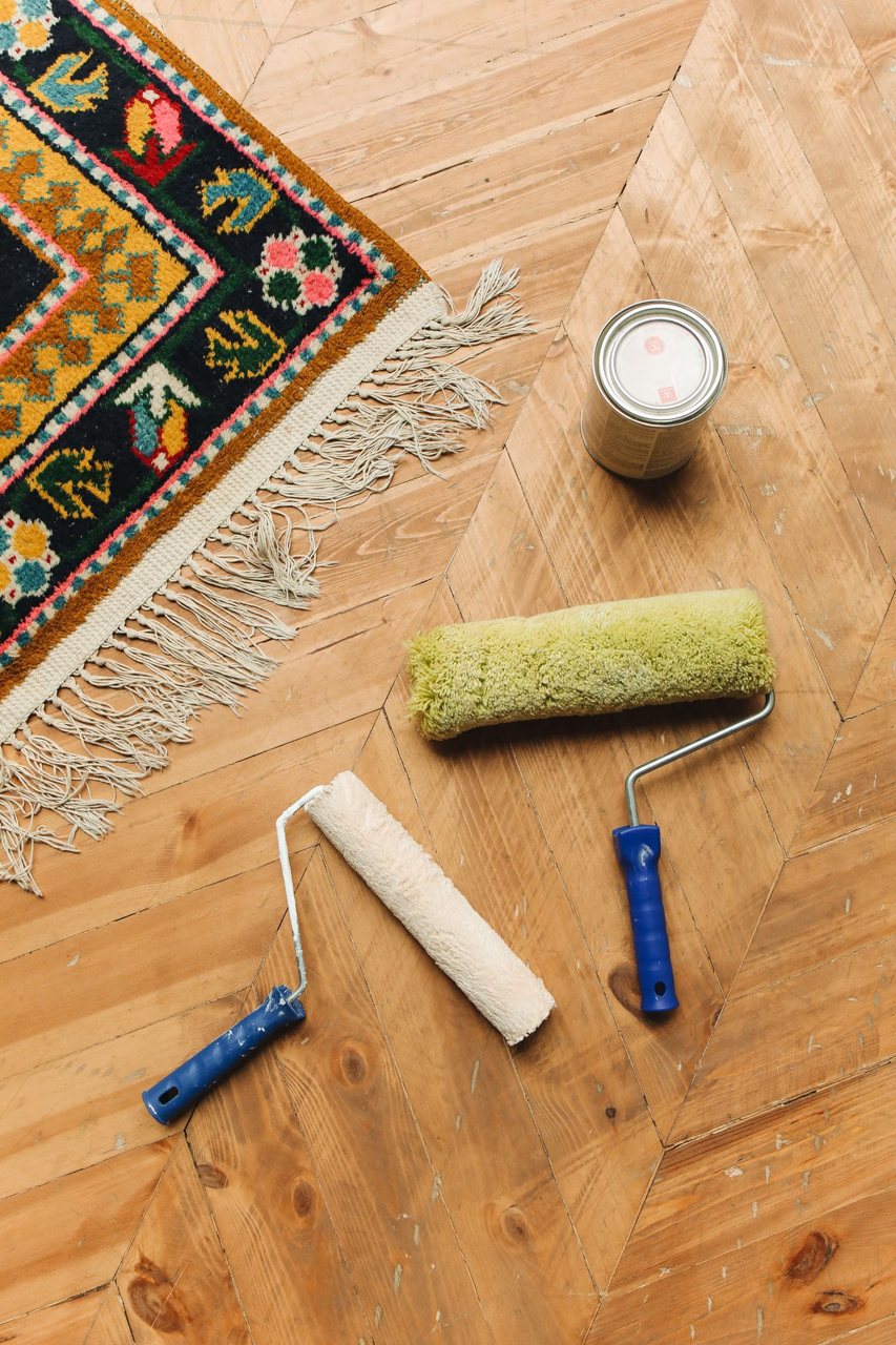 Free A decorative rug on wooden flooring with paint rollers and a can for home renovation. Stock Photo